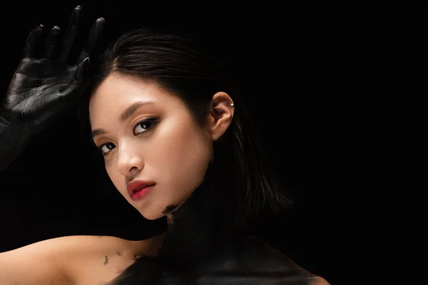 Brunette asian woman with bare shoulders and hand in paint looking at camera isolated on black — Foto stock