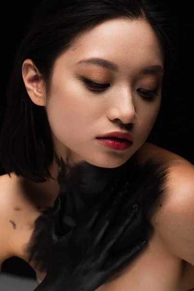 Young asian woman with naked shoulders and hand in paint touching body isolated on black — Stock Photo