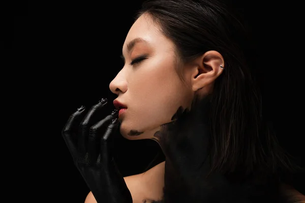Side view of young asian woman with hand in paint touching lip isolated on black — Stockfoto