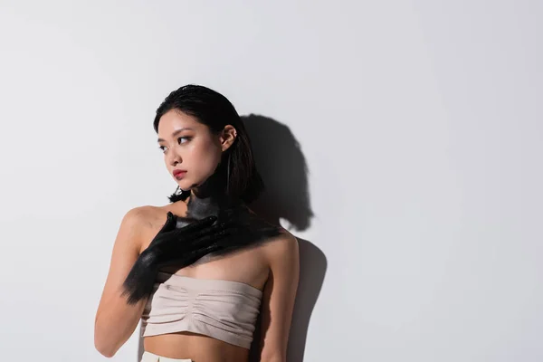 Young asian woman with bare shoulders and hand in black paint touching chest on white — Stock Photo