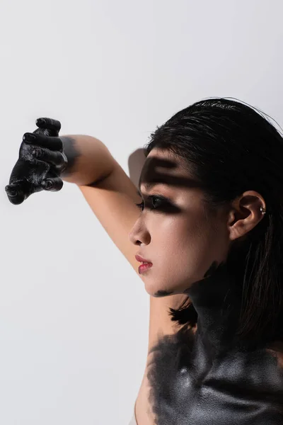 Side view of young asian woman with bare shoulders and hand in black paint above face on white — Stock Photo