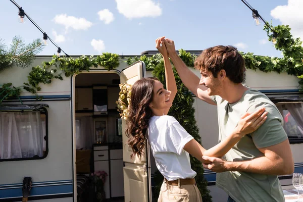 Side view of smiling couple holding hands near camper outdoors — Stock Photo