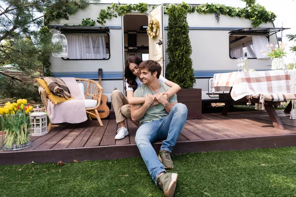 Smiling woman embracing boyfriend on terrace near camper outdoors — Foto stock