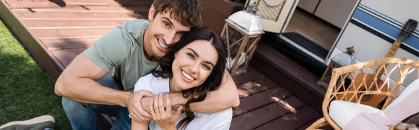 Positive young couple looking at camera while embracing on terrace of camper, banner — Stock Photo