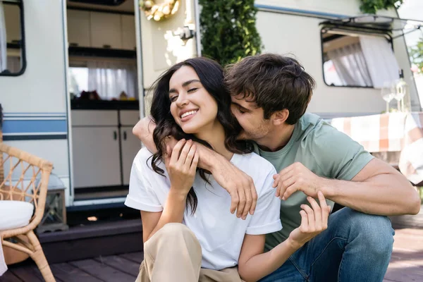 Young man kissing smiling girlfriend on terrace of camper van — Foto stock