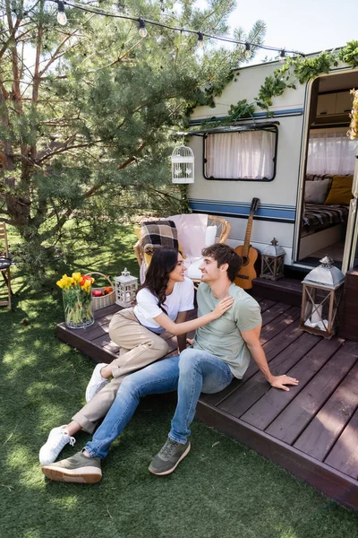 Side view of smiling woman touching boyfriend on terrace of camper van - foto de stock