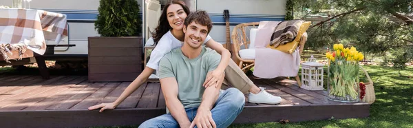 Positive young couple looking at camera near camper, banner - foto de stock