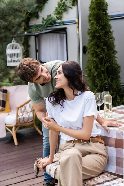 Smiling man hugging girlfriend near wine on terrace of camper van — Fotografia de Stock