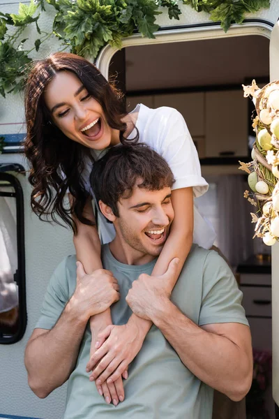 Positive brunette woman embracing boyfriend near camper van outdoors — Stock Photo