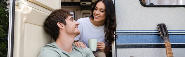 Smiling woman holding cup and hugging boyfriend near acoustic guitar and camper van, banner — Foto stock
