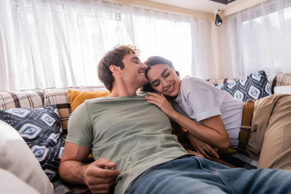 Young woman hugging boyfriend while lying on bed in camper van — Stock Photo