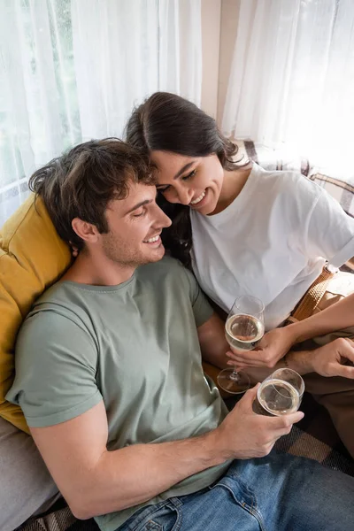 High angle view of cheerful young couple holding glasses of wine on bed in camper van — Foto stock