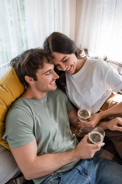 High angle view of cheerful young couple holding glasses of wine on bed in camper van - foto de stock