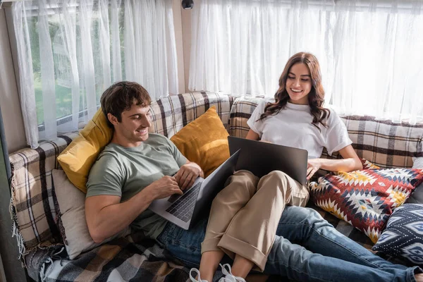 Smiling couple using laptops on bed in camper van — Photo de stock