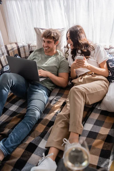 Smiling couple using devices on bed in camper van — Photo de stock