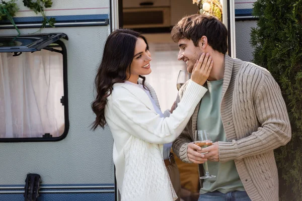 Smiling woman touching boyfriend with glass of wine near camper van — стоковое фото