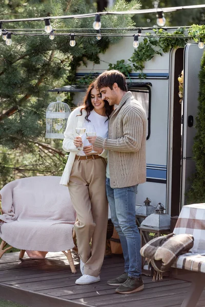 Smiling couple in cardigans toasting with wine near camper van outdoors — Photo de stock