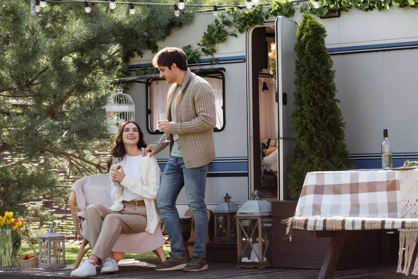 Smiling man in cardigan standing near girlfriend with wine and camper van — Stockfoto