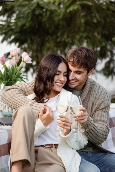 Positive man holding wine near brunette girlfriend in cardigan outdoors — стоковое фото