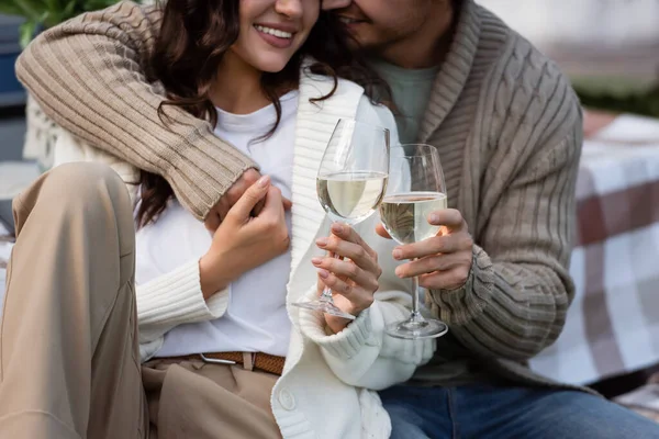 Cropped view of smiling couple in cardigans holding hands and glasses of wine outdoors — стоковое фото