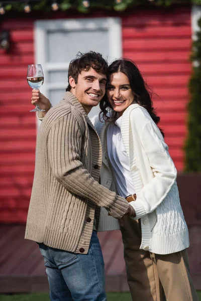 Smiling woman holding glass of wine and holding hand of boyfriend in cardigan outdoors — Stockfoto