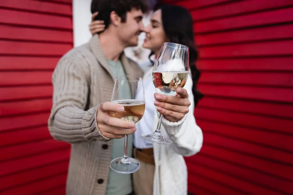Blurred young couple kissing and holding glasses of wine near house — стоковое фото