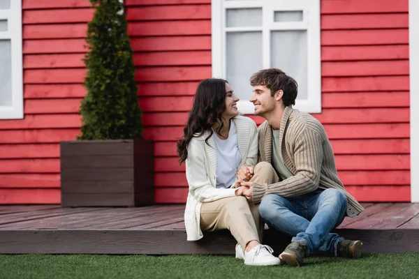 Side view of young couple in warm cardigans holding hands near blurred house — Stock Photo