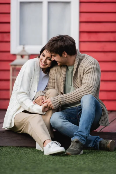 Smiling couple in warm cardigans holding hands on terrace of house — стоковое фото