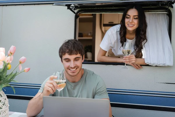 Smiling couple with wine using laptop near camper van — Foto stock