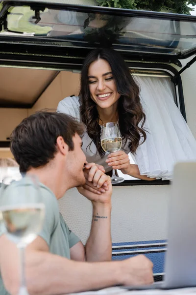 Усміхнений чоловік цілує руку дівчини у фургоні біля лози та ноутбука на відкритому повітрі — стокове фото