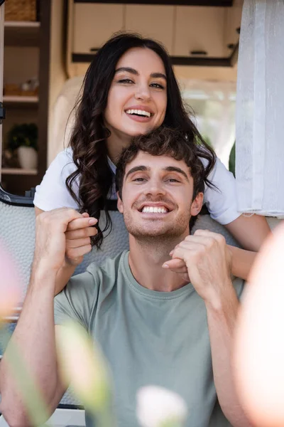 Happy young couple holding hands and smiling at camera near camper van — стоковое фото