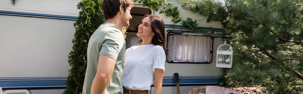 Cheerful brunette woman looking at boyfriend on terrace near camper van, banner — Stock Photo