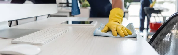 Vista recortada del limpiador en el escritorio de lavado de guantes de goma cerca del monitor de la computadora y la tableta digital, pancarta - foto de stock