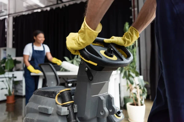 Cropped view of man in rubber gloves operating floor scrubber machine near blurred bi-racial woman — Stock Photo