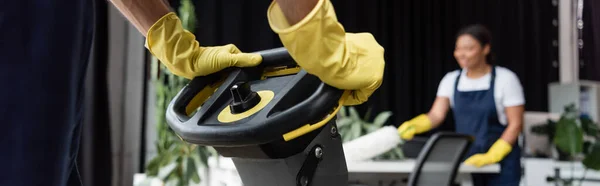 Vue recadrée de l'homme en gants de caoutchouc près de la machine de nettoyage de sol et femme bi-raciale sur fond flou, bannière — Photo de stock