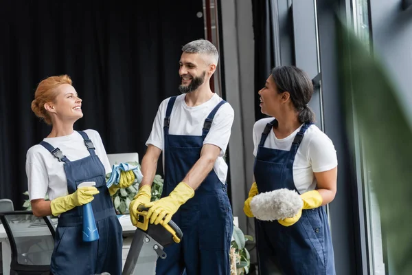 Aufgeregtes multiethnisches Team professioneller Reinigungskräfte, die im Büro reden und lachen — Stockfoto