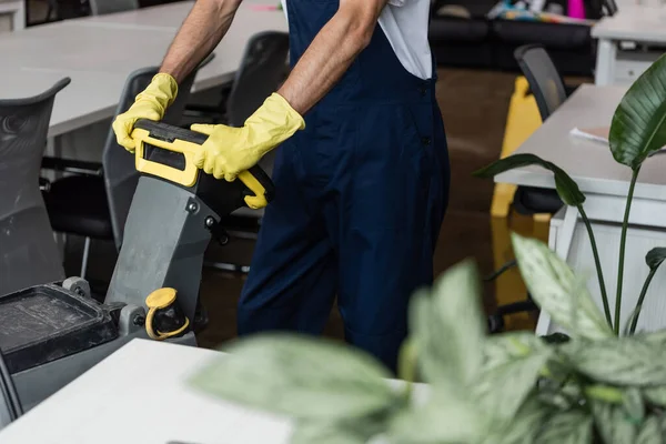 Vista recortada del hombre en monos y guantes de goma que trabajan con la máquina de fregar piso - foto de stock