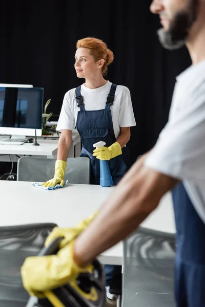 Eine lächelnde Frau blickt weg, während sie neben einem Mann im verschwommenen Vordergrund den Schreibtisch wäscht — Stockfoto