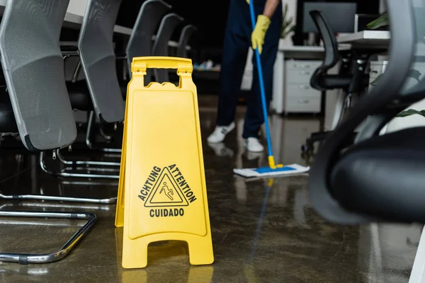 Cropped view of blurred cleaner washing floor near attention sign board — Stock Photo