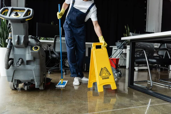 Vue recadrée de l'homme avec la serpillière tenant le panneau d'avertissement près de la machine d'épurateur de sol — Photo de stock
