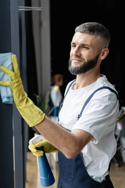 Sorridente barbudo homem limpeza escritório com detergente e pano — Fotografia de Stock