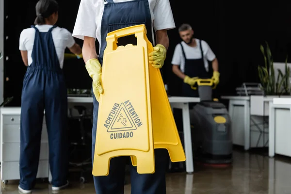 Frau mit Warntafel neben Kollegen auf verschwommenem Hintergrund — Stockfoto