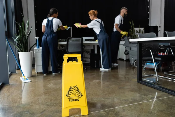 Placa sinal de atenção perto de equipe profissional multiétnica limpeza escritório moderno — Fotografia de Stock