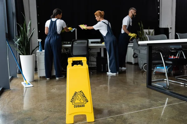 Attention sign board near multiethnic professional team cleaning modern office — Stock Photo