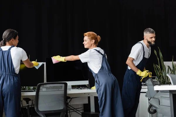Interracial women wiping computer monitors near man with floor scrubber machine — Stock Photo