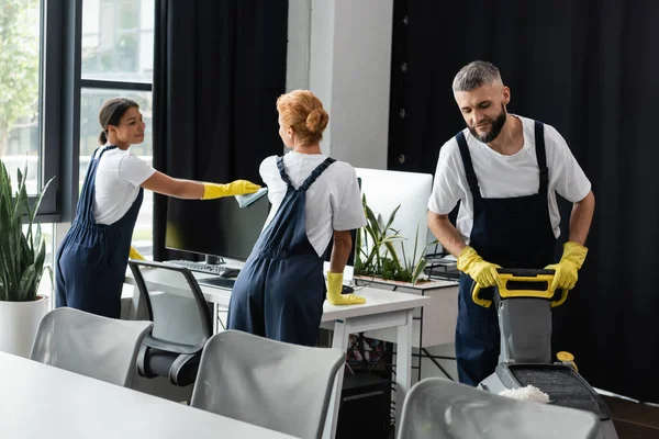 Junge Frau wischt Computermonitor in der Nähe von Kollegen ab, die Büro putzen — Stockfoto