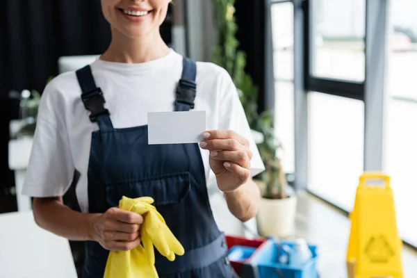 Обрезанный вид улыбающейся женщины в комбинезоне с пустой визиткой — стоковое фото