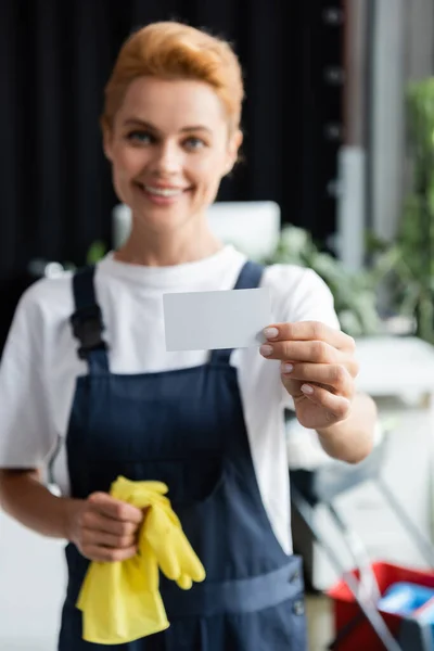 Blurred professional cleaner showing empty business card while smiling at camera — Stock Photo