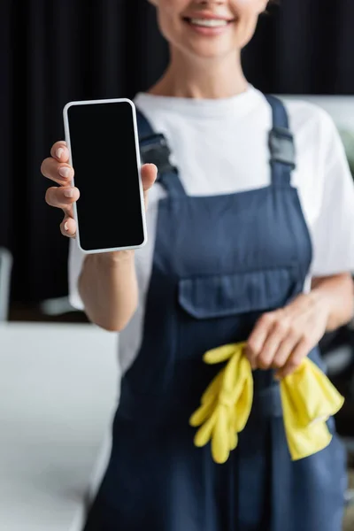 Visão parcial da mulher desfocada em macacões segurando luvas de borracha e smartphone com tela em branco — Fotografia de Stock