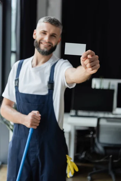 Selective focus of empty business card in hand of smiling professional cleaner — Stock Photo